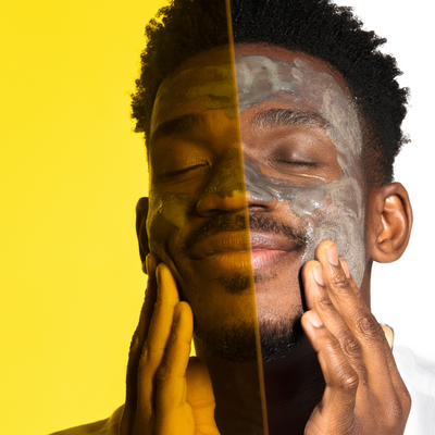 Close-up of a man with a facial mask applying skincare product, half of his face shown through a yellow-tinted transparent panel.