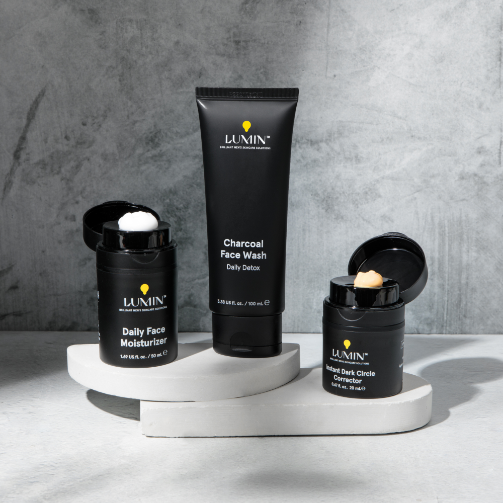 Lumin men's skincare set with Daily Face Moisturizer, Charcoal Face Wash, and Instant Dark Circle Corrector on white platforms