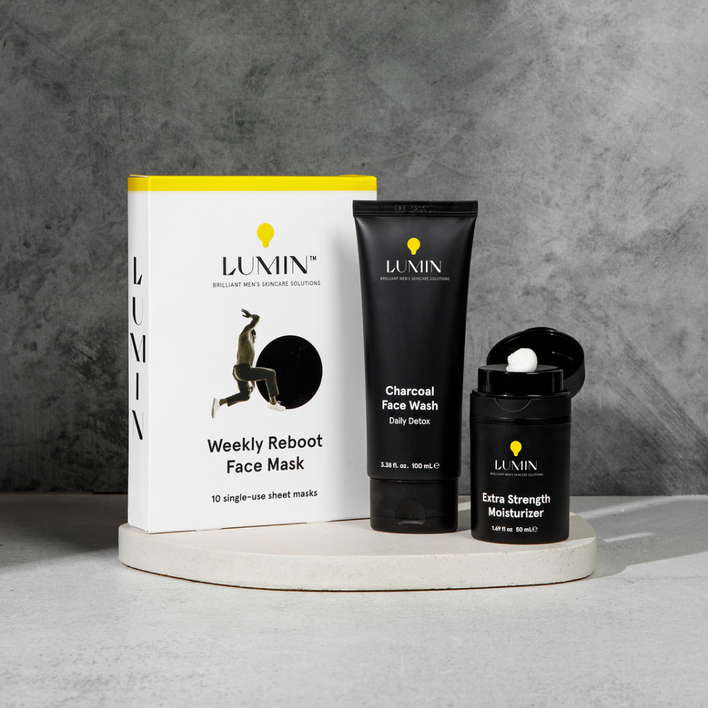 Lumin men's skincare set with Weekly Reboot Face Mask, Charcoal Face Wash, and Extra Strength Moisturizer on white platform.