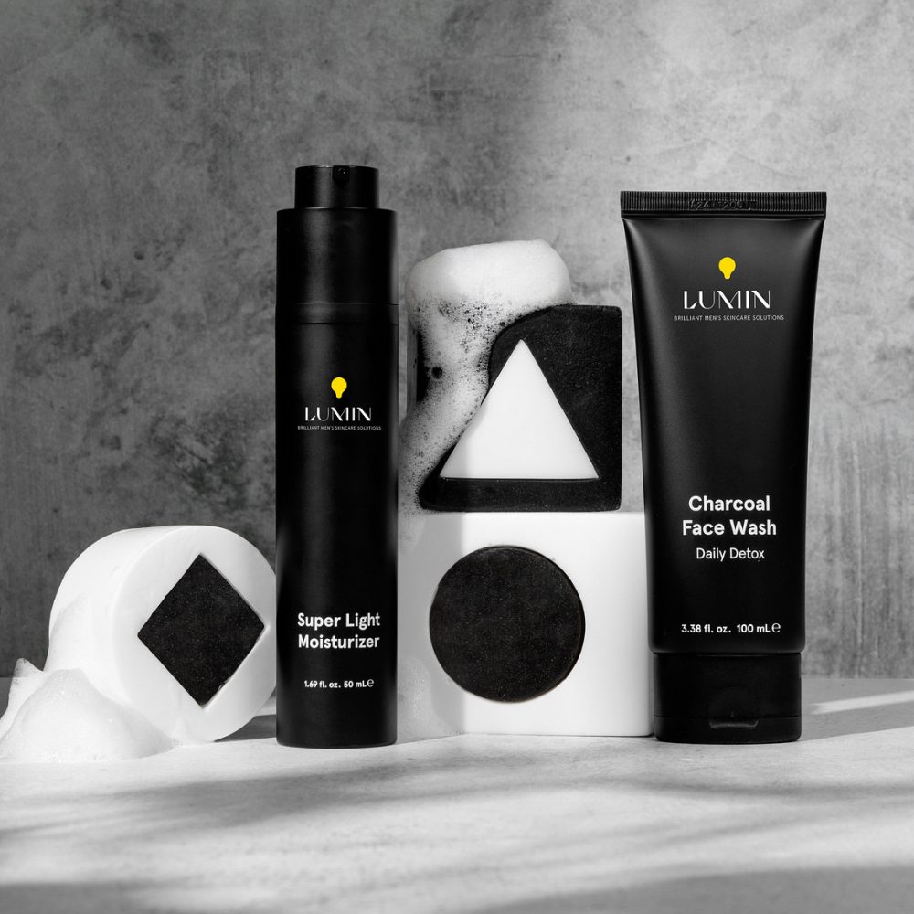 Lumin men's skincare Super Light Moisturizer and Charcoal Face Wash with geometric soap bars and foam on concrete surface.