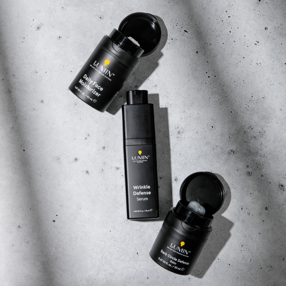 Lumin black skincare bottles and jars on concrete surface: Daily Face Moisturizer, Wrinkle Defense Serum, Dark Circle Defense Balm.