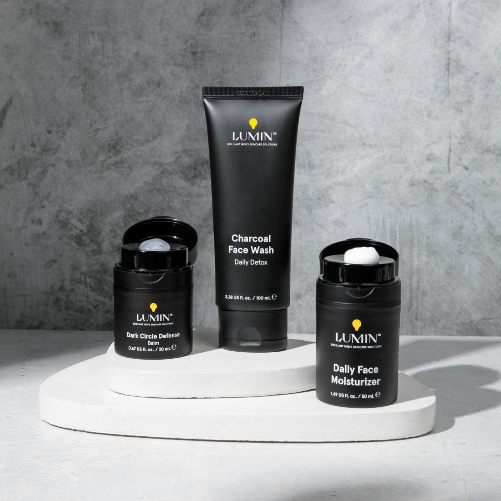 Lumin men's skincare set with Charcoal Face Wash, Dark Circle Defense Balm, and Daily Face Moisturizer on white stand