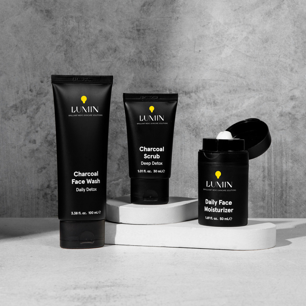 Lumin men's skincare trio with charcoal face wash, charcoal scrub, and daily face moisturizer on white platforms.
