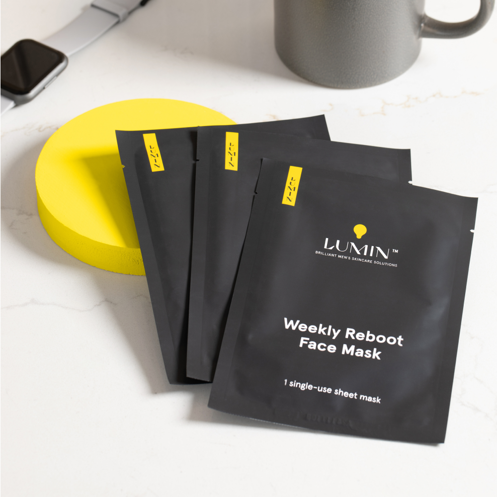 Lumin Weekly Reboot black sachets of single-use men's face masks on white marble surface with yellow round prop.