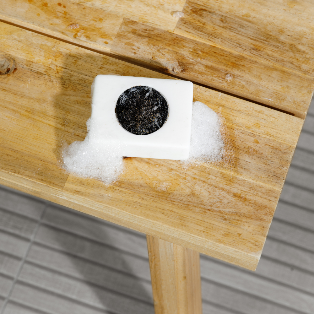 White cleaning sponge with black scrub pad and soap suds on wooden table, natural wood surface, cleaning tools