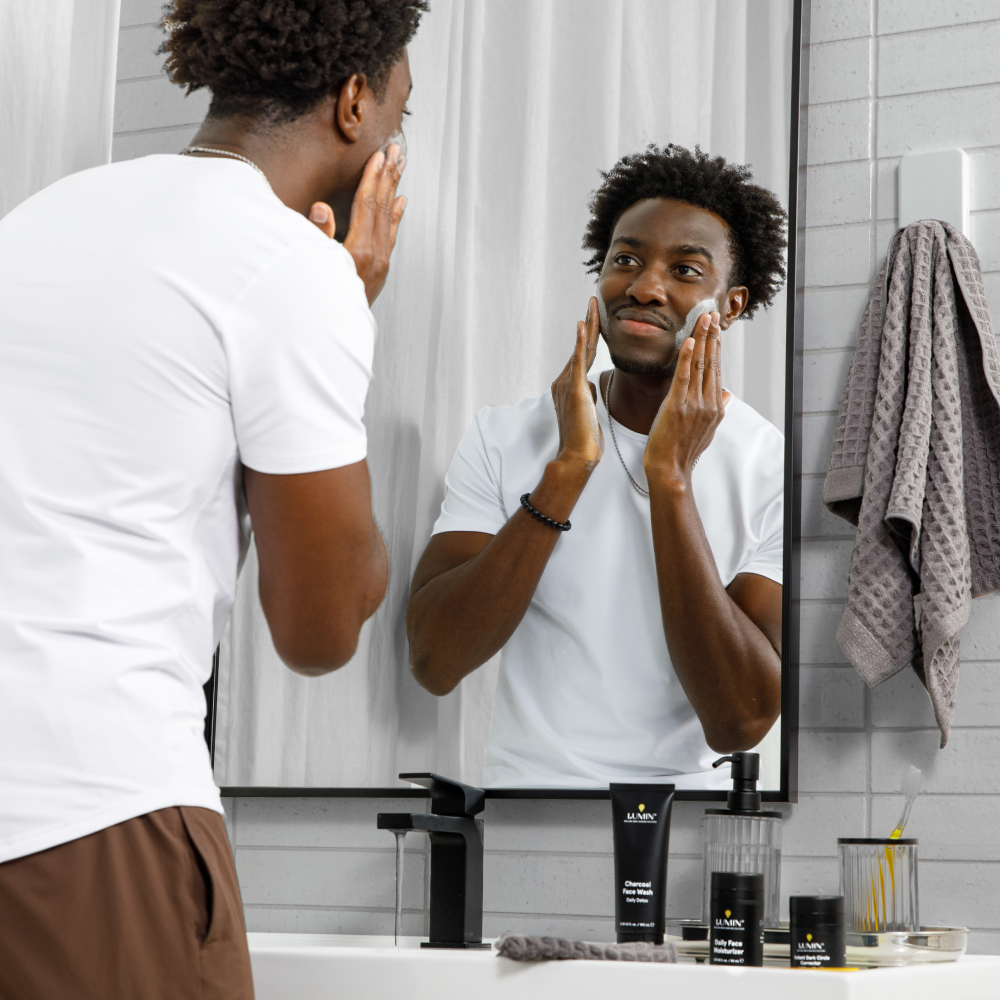Man applying face wash in bathroom mirror with Lumin charcoal face wash and moisturizer skincare products on sink.
