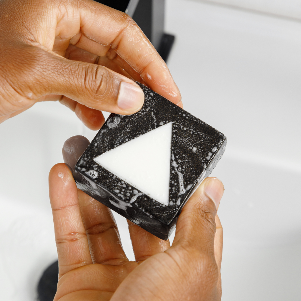 Black and white triangular design hand soap bar with bubbles held over white bathroom sink, skincare product