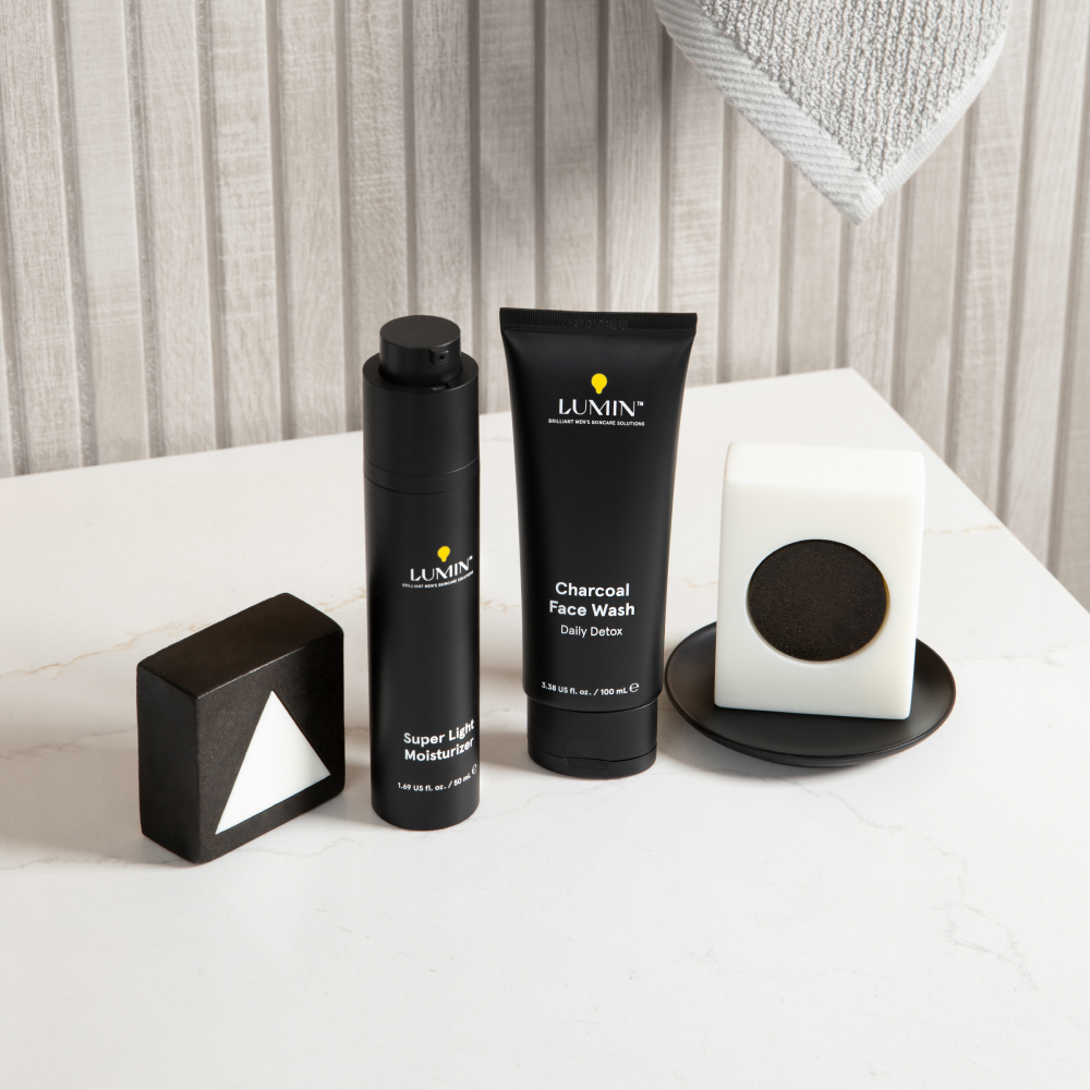 Lumin men's skincare set with super light moisturizer, charcoal face wash, and geometric black and white soap bars on marble counter.