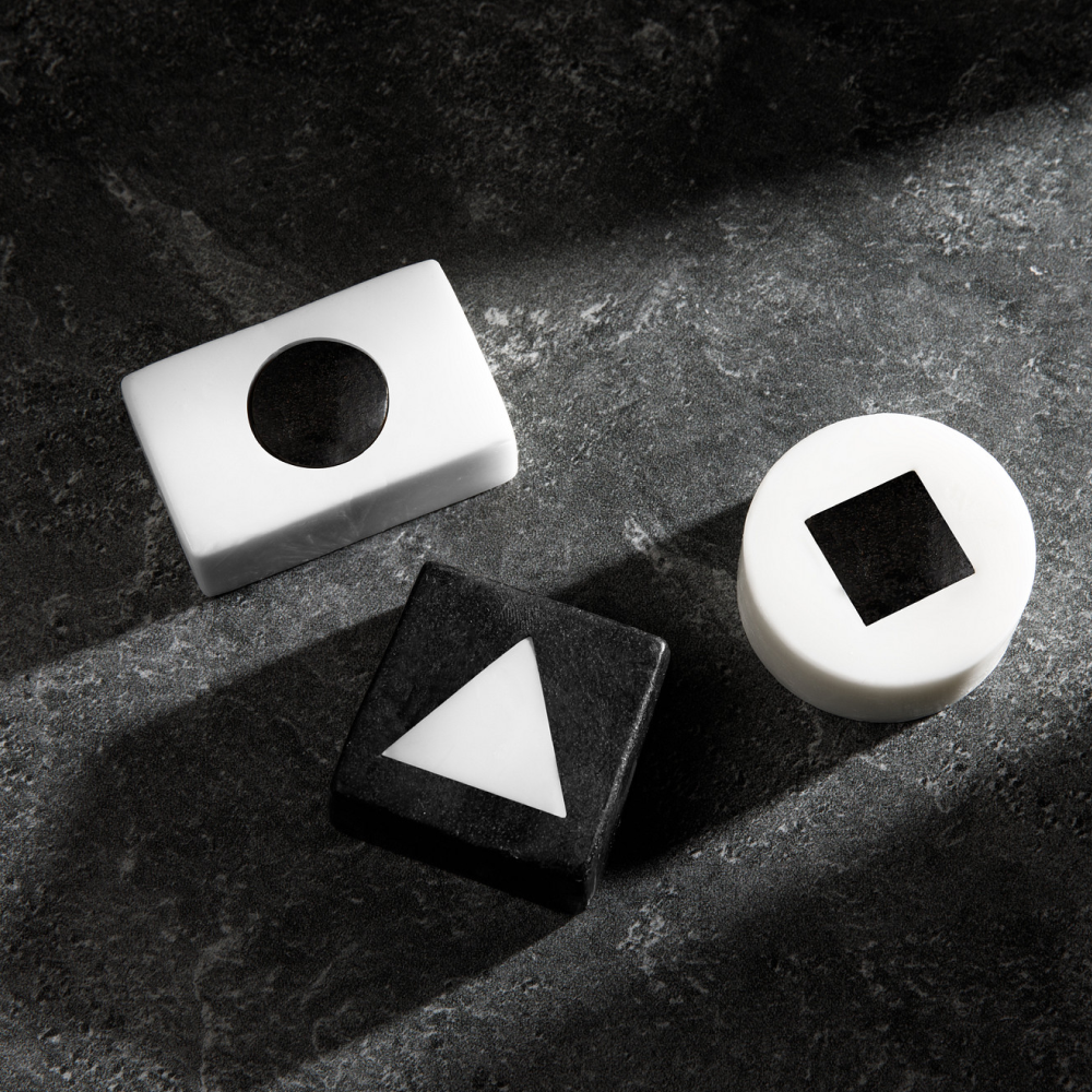 Black and white geometric blocks with cutout shapes including circle, triangle, and square on textured dark surface.