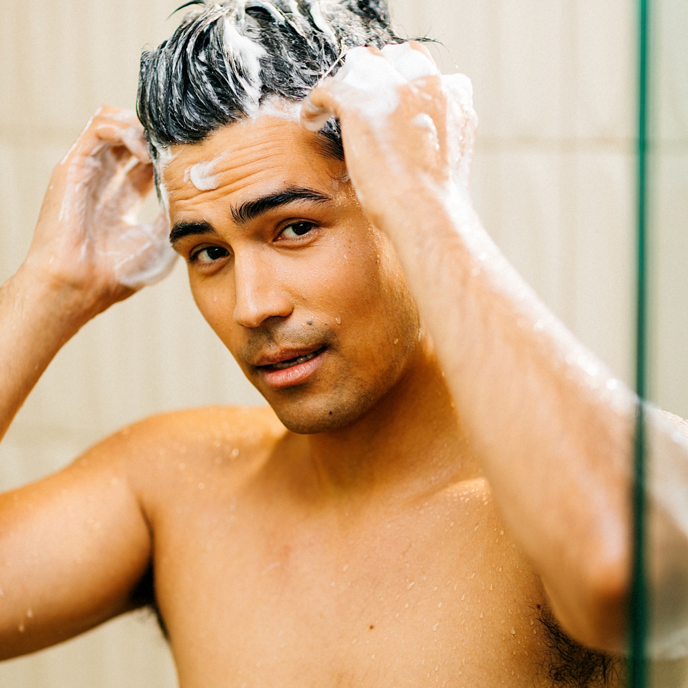 Young man washing hair with shampoo lather in shower, skincare routine, wet skin, men's grooming, personal hygiene care