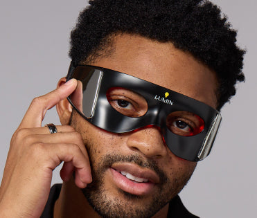 Close-up of a man wearing a sleek black and red eye mask from a men's skincare brand.